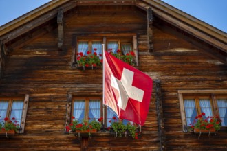 Beautiful Old Town with a Wood House with Flower and Swiss Flag in a Sunny Summer Day in Andermatt,