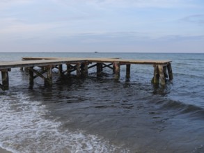 An old wooden jetty juts into the sea, surrounded by gentle waves under an evening sky, sopot,