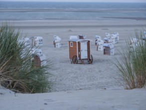 Beach section with scattered beach chairs, sand dunes and grass under a twilight sky by the sea,