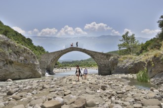 Two young woman walking barefoot in the riverbed over large stones, Ottoman stone bridge, Kadiut