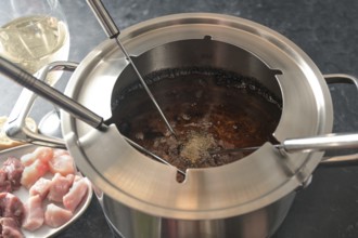 View into a fondue pot with boiling hot oil, long forks, pieces of meat and wine, festive dinner