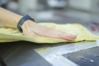 A hand wiping a car surface with a yellow cloth during cleaning