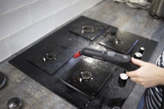 Focused steam cleaning of a black stovetop area in the kitchen