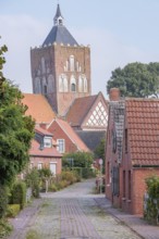 Historic village street with brick houses and a large tower in the background, krummhörn, east