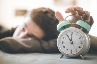 White alarm clock in the morning. Young man wakes up