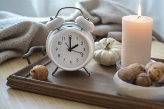 White vintage alarm clock, candle, autumn decoration and sweets on a nightstand with a natural