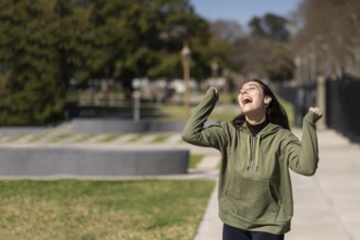 Young girl wearing sportswear celebrates in the park smiling screaming and with arms raised