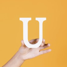 Female hand holding white uppercase alphabet u yellow surface