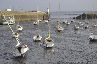 Saint Quay Portrieux, Sailboats rest on mud flats during low tide in a serene harbor with a distant