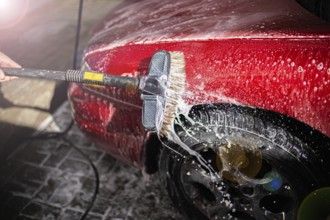 Washing a soapy red car focusing on the side and tire with a brush