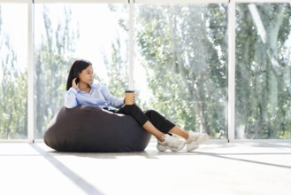 Pretty african american business woman relaxing on bean bag chair with cup of coffee on panoramic