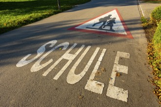Triangular sign with children and the word SCHOOL on a street in front of the village school,