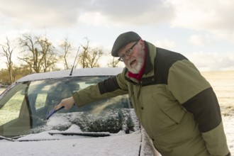 Senior citizen removes frost and snow from car windscreen