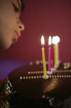 Little girl blowing birthday chocolate cake candles in a row over red background