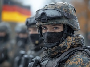 A masked soldier stands with her unit, wearing a helmet in a winter setting, with the German flag