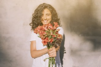 Young woman standing against wall holding (alstroemeria) red flower bouquet hands