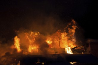 Arson or nature disaster, burning fire flame on wooden house roof