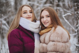 Two happy female friends enjoying snowing weather outdoors, women best friends in winter clothes