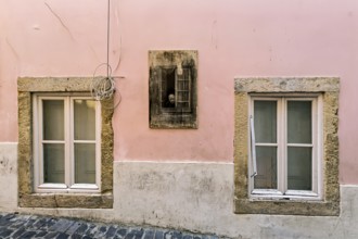 Facade of an old building with pastel pink walls and stone-framed windows with closed wooden