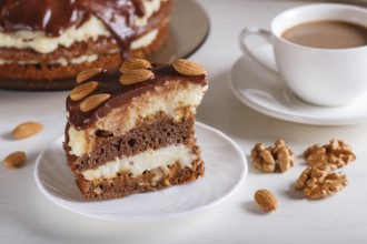Homemade chocolate cake with milk cream, caramel and almonds on white wooden background. cup of