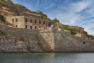Dilapidated-looking old buildings on a rocky coastline surrounded by clear skies and calm seas,
