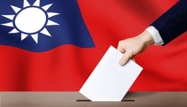 Taiwan presidential election. Hand holding ballot in ballot box with Taiwan flag in background