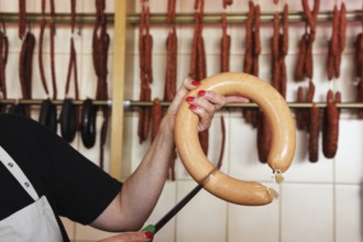 Saleswoman in the butcher's shop holds a knife to a sausage