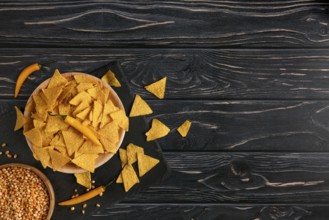 Bowl of tortilla chips next to raw sweetcorn and yellow peppers on a dark wooden table