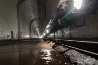 Deep tunnel with wet concrete walls and light at the end, industrial ambience, Rappbodetalsperre,