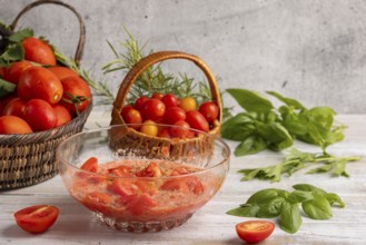 Glass bowl with prepared tomato sauce and sliced tomatoes, surrounded by fresh tomatoes in baskets,