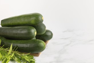 Fresh courgettes stacked on a wooden board with fresh herbs against a light-coloured background