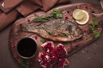 Gebratener Doradenfisch, mit Gewürzen und Kräutern, auf einem Holzbrett, Granatapfelsauce,