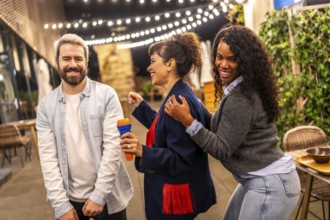 Multi-ethnic happy friends dancing while singing karaoke in the terrace of a bar