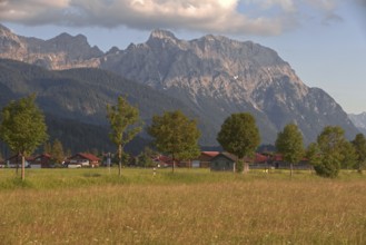 View of a village in front of majestic mountains, surrounded by green meadows and trees under a