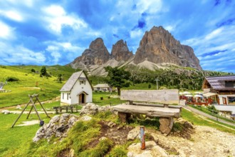 Picturesque landscape featuring a wooden bench, a small chapel, and the majestic peaks of the sella