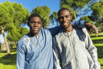 Two young senegalese men wearing traditional dashiki clothing embrace in a park, celebrating