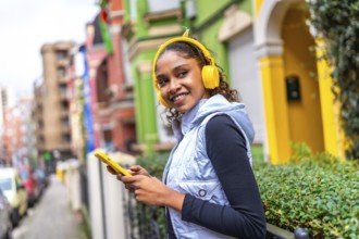 Confident african american woman using phone and listening to music walking next a multicolored