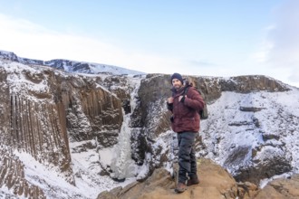 Portrait of a hiker at frozen Hengifoss waterfall in cold Iceland winter, volcanic cliffs