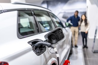 Couple looking at a charging electric car in a dealership, embracing sustainable transportation