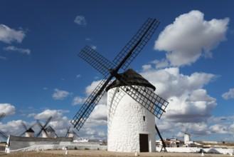 A historic white windmill against a blue sky with clouds and sunshine in a vast landscape,