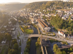 Aerial view of a town with a river surrounded by hills and green vegetation at sunset, centred on a