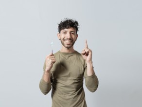 Smiling young man holding dental brush pointing up. Handsome guy holding toothbrush pointing an
