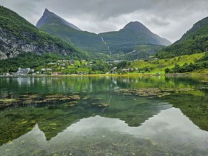 Mountainous landscape with a calm fjord reflecting the surrounding mountains and village,