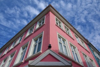 Historic building with pink facade and white window frames under a blue sky with light clouds,