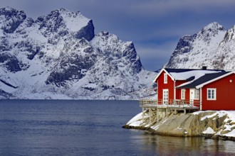 Red house by the fjord in front of snow-covered mountains in a wintry landscape, Scandinavian style