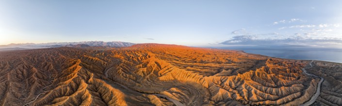 Panorama, landscape of eroded hills, badlands at sunrise, Issyk Kul Lake in the background, aerial