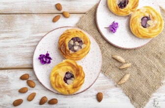 Small cheesecakes with jam and almonds with cup of coffee on a white wooden background and linen