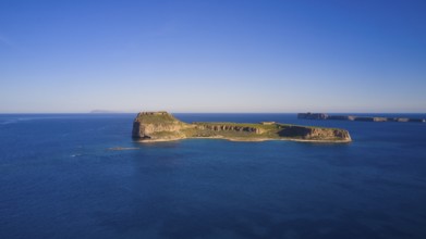 Drone shot, A deserted island in the vast blue ocean with rocky coastlines and clear skies,