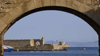 View through a stone window arch to the sea and a small castle in the background, De Naillac Tower,