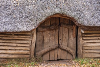 Entrance to a longhouse built of tree logs and a detached roof of reeds